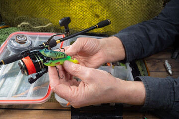 Sport fishing equipment on a table in a studio composition, against a background of a net. A fisherman's hands check the tackle for use.