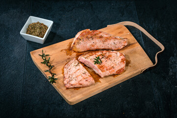 Angeschnittenes Secreto vom Schwein auf Holzbrett mit Messer, Thymian und Grillgew&uuml;rz auf scharzem Schiefer