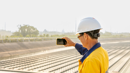 Obraz premium Construction Worker Taking Mobile Phone Pictures of Solar Panels at Renewable Energy Site During Golden Hour in Urban Area