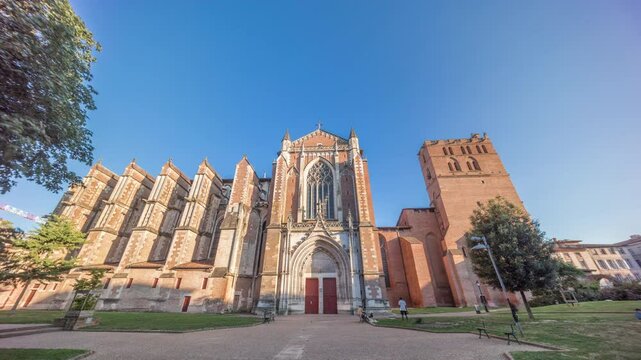 Saint Etienne Cathedral in Toulouse timelapse hyperlapse. Details of the north facade of church. Sunset shadows cover its walls, with a green park in front and a blue sky above. France.