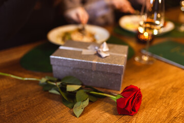 Romantic dinner date. Boyfriend gifts his girlfriend red rose and gift on a romantic dinner for...