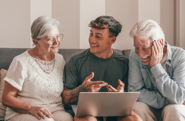 Cheerful Multi generation family of grandparents and young grandson share social media on laptop...