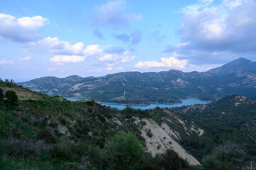 Majestic hills embrace the tranquil lake under a canvas of soft, fluffy clouds at dusk