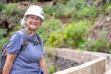 Smiling senior hiker woman in protective helmet sitting to rest during an hike on top of a...