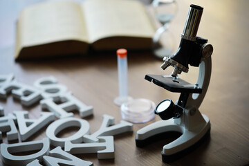 Microscope on Wooden Desk with Laboratory Equipment and Open Book in Background