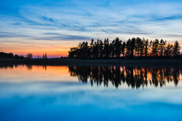 Fototapeta premium Reflection of trees at Lake Vanern in Sweden during tranquil sunset hues with a serene atmosphere