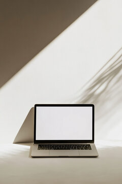 Fototapeta sleek laptop with blank screen is placed on white surface, illuminated by soft natural light and casting shadow