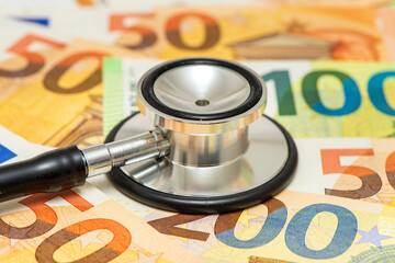 Ein medizinisches Stethoskop liegt auf vielen Euro Banknoten als Symbol für Kosten im...