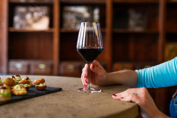 A woman holding a glass of red wine at a stylish tasting session, with gourmet appetizers on a...