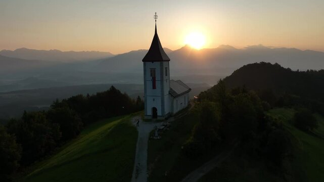 Rising-up drone shot of the Saint Primus and Felician Catholic Church at sunset in Jamnik, Slovenia