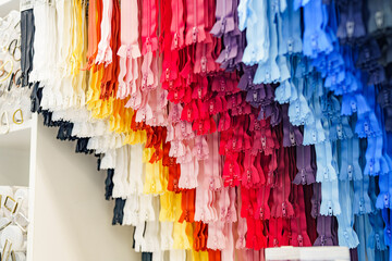 Fototapeta premium Sewing zippers of different colors hang in a shop window.