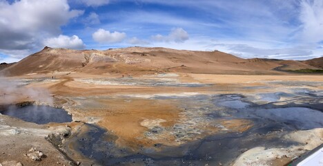 barren landscape of a geothermal area with soil in the colors of orange, yellow, blue, grey, white 