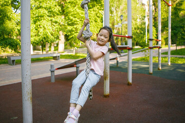 Little Girl Cheerful Smiling While Climbing Rope At Outdoor Playground