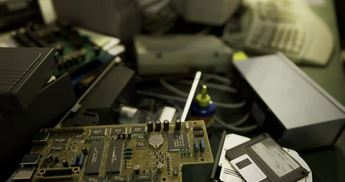 Various old computer parts, including circuit boards and floppy disks, are scattered across a workbench in a messy workshop, reflecting a retro technology atmosphere.