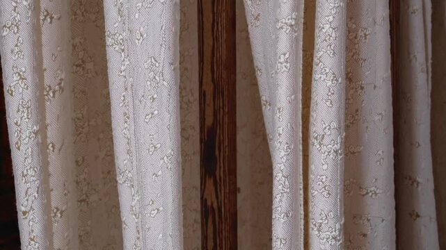 Delicate white curtain featuring intricate floral pattern gracefully hanging from rustic wooden rod, filtering soft light in elegant interior space