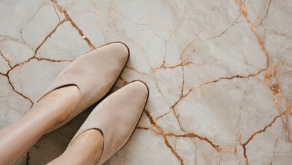 A person standing on a marble floor with beige shoes, informative and clear description