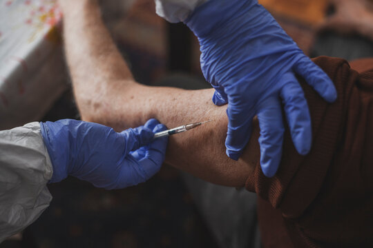 Doctor in protective suit vaccinating elderly man at home during epidemic