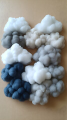 Fluffy clouds in shades of white gray and blue arranged on a tan surface create a whimsical and soft textured compo