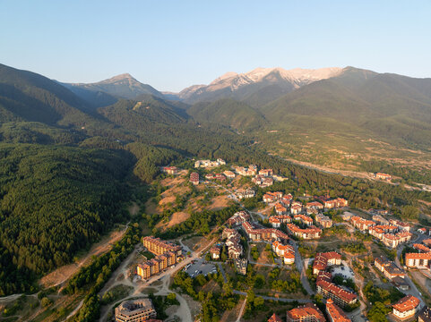 Sunset over Bansko, Bulgaria, with golden light illuminating rooftops and surrounding mountains. Aerial view captures warm evening glow, peaceful atmosphere, and breathtaking natural scenery. Travel