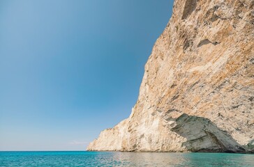 Fototapeta premium Bright sun illuminates towering cliffs above serene blue waters, showcasing the natural beauty of Greece in a peaceful summer landscape ideal for relaxation and exploration