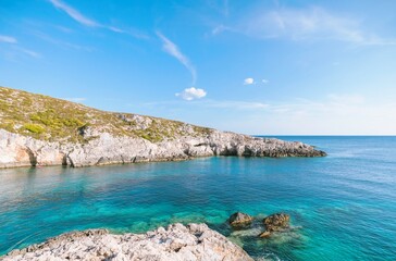 Fototapeta premium Bright sunlight illuminates the serene turquoise waters alongside the rugged coastline of Greece. Lush greenery adorns the cliffs, creating a perfect summer getaway for relaxation and exploration