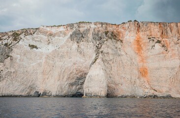 Rocky cliffs rise dramatically along the coast of Greece, highlighted by summer lighting. Calm...