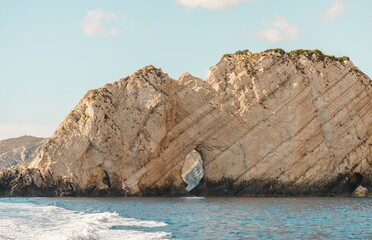 Naklejka premium Guests enjoy a boat trip in Greece, marveling at unique rock formations and natural arches along the coastline under a clear blue sky during summer, creating a perfect getaway experience