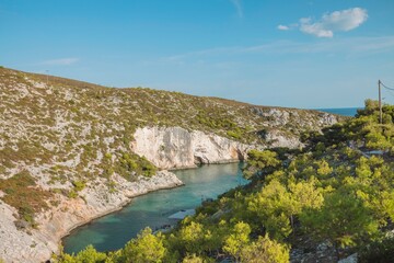 Turquoise waters embrace a hidden cove in Greece, surrounded by lush greenery and rocky cliffs. Sunlight creates a tranquil atmosphere perfect for relaxation and exploration