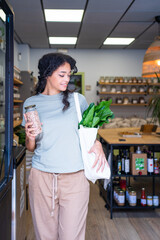 Young woman holding reusable bag and jar with legumes at zero waste store