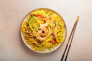Delicious pad thai dish with shrimps, peanuts, lime and chopped vegetables, chopsticks on light beige background top view, Thai food
