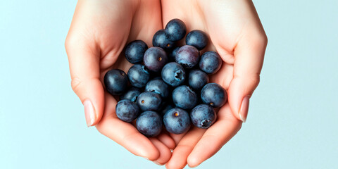 Handful of fresh ripe blueberries held in cupped hands on soft blue background, symbolizing healthy snacking and natural antioxidants