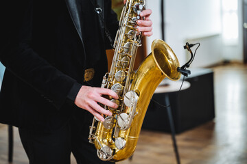 Obraz premium A man dressed in a stylish formal suit skillfully plays a saxophone while standing next to a microphone, producing a captivating melody that beautifully resonates throughout the entire room