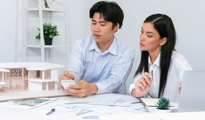 Professional male asian architect using ruler to measure house model length while young beautiful...