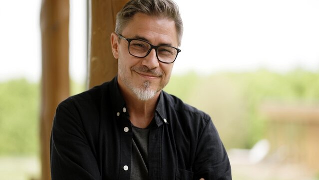 Portrait of happy casual middle age man in glasses standing on balcony at home relaxing, smiling.