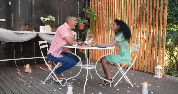 Diverse couple holding hands in garden candlelit dinner, sharing intimate conversation