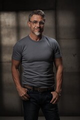 Portrait of confident mature man in casual standing on gray background. Older middle aged guy in eyeglasses smiling. Healthy active, fit mid adult male in 50s.