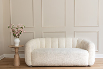 white boucle loveseat against cream colored wall with wainscotting and a small table with cherry blossom branches, room for copy
