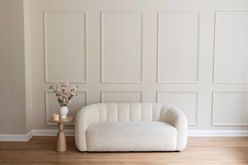 white boucle loveseat against cream colored wall with wainscotting and a small table with cherry blossom branches, room for copy