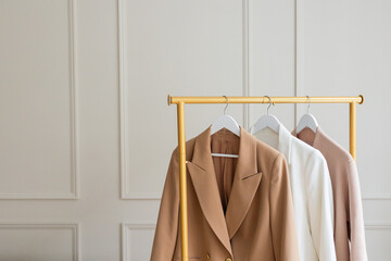 Three womens' blazers in light neutral colors hanging from a gold rack