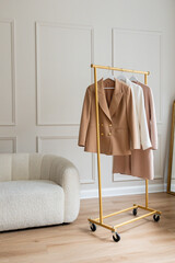 Three womens' blazers in light neutral colors hanging from a gold rack