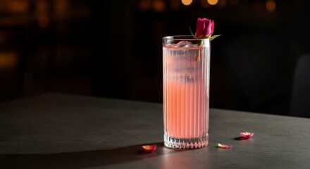 Refreshing pink cocktail with rose garnish on dark surface