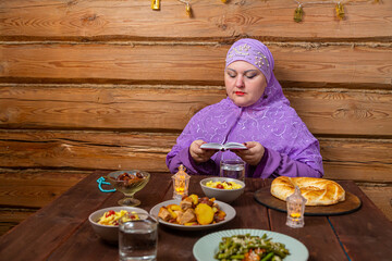 Muslim woman in purple hijab reads dua at festive table Eid al-Fitr