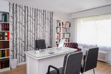 General view of the doctor's office of a medical consultation or an ambulatory or private health center. There are shelves with anonymous medicine books, a computer and chairs for doctor and patients