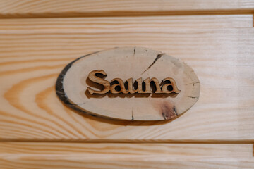 Wooden “Sauna” sign mounted on a light wood plank wall, rustic and natural in style, indicating...