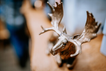 Bronze moose figurine with large antlers placed on a wooden surface, captured in a rustic interior setting with shallow depth of field for artistic focus..