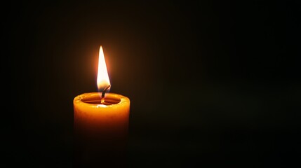 Burning candle with yellow light illuminates a dark background casting