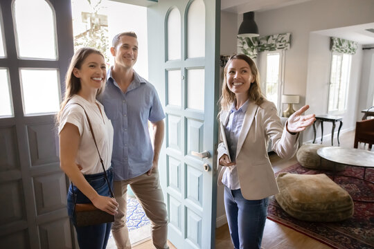 Positive, real estate agent welcoming young married couple into house for sale or renting, showcasing new property, provide professional services during formal meeting. Homeownership, consultation - Powered by Adobe