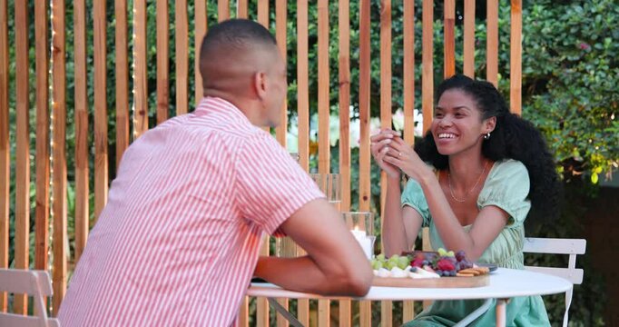 Diverse couple enjoying in garden date, sharing fruit platter at cozy cafe table