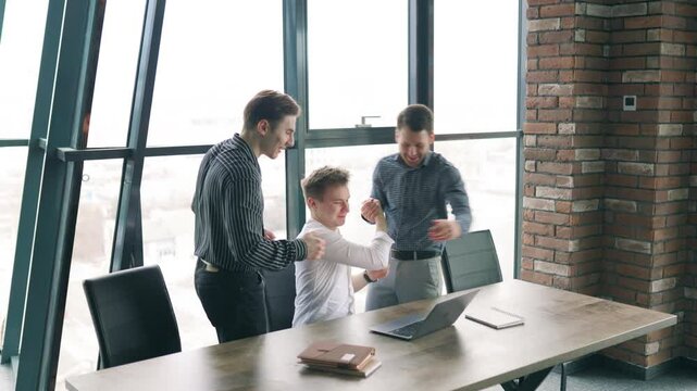 Celebrating teamwork and success in a modern office setting with young professionals collaborating on laptops