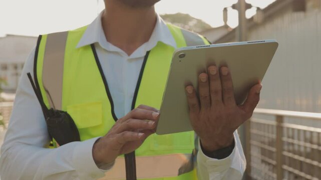 Taskmaster in safety vest inputs data in tablet computer checking construction site processes closeup. Skilled engineer hands hold device controlling infrastructure development